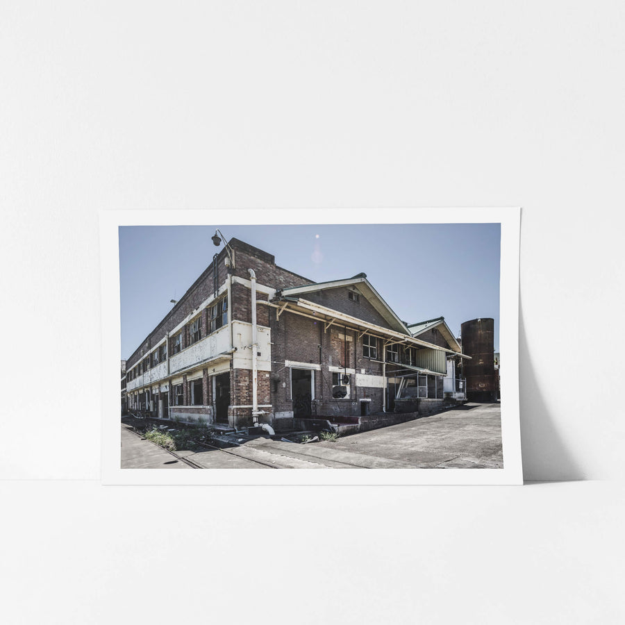 Southeastern Corner at Peters Ice Cream Factory, two storeys of brown brick rise against a flat blue sky.