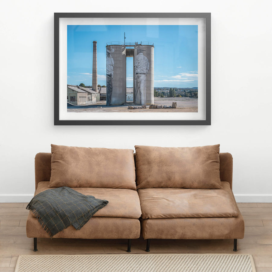 Between Silos at Portland Cement Works, two concrete silos stand side by side on bare ground, a narrow vertical gap cut.