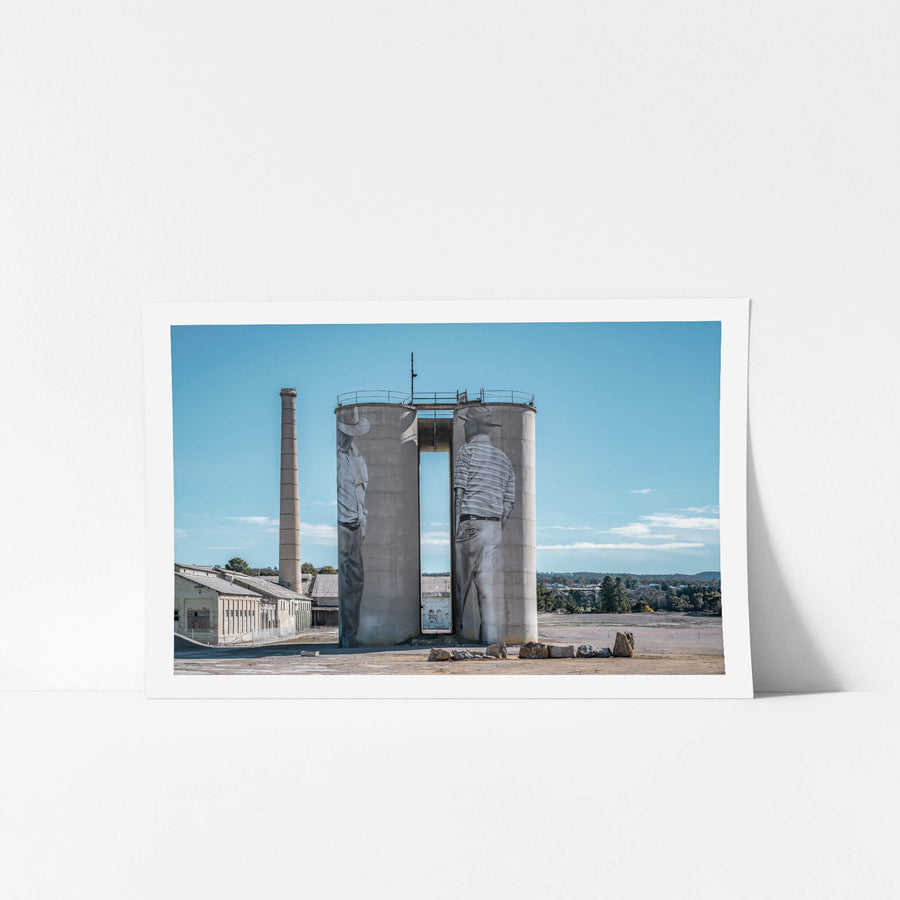 Between Silos at Portland Cement Works, two concrete silos stand side by side on bare ground, a narrow vertical gap cut.