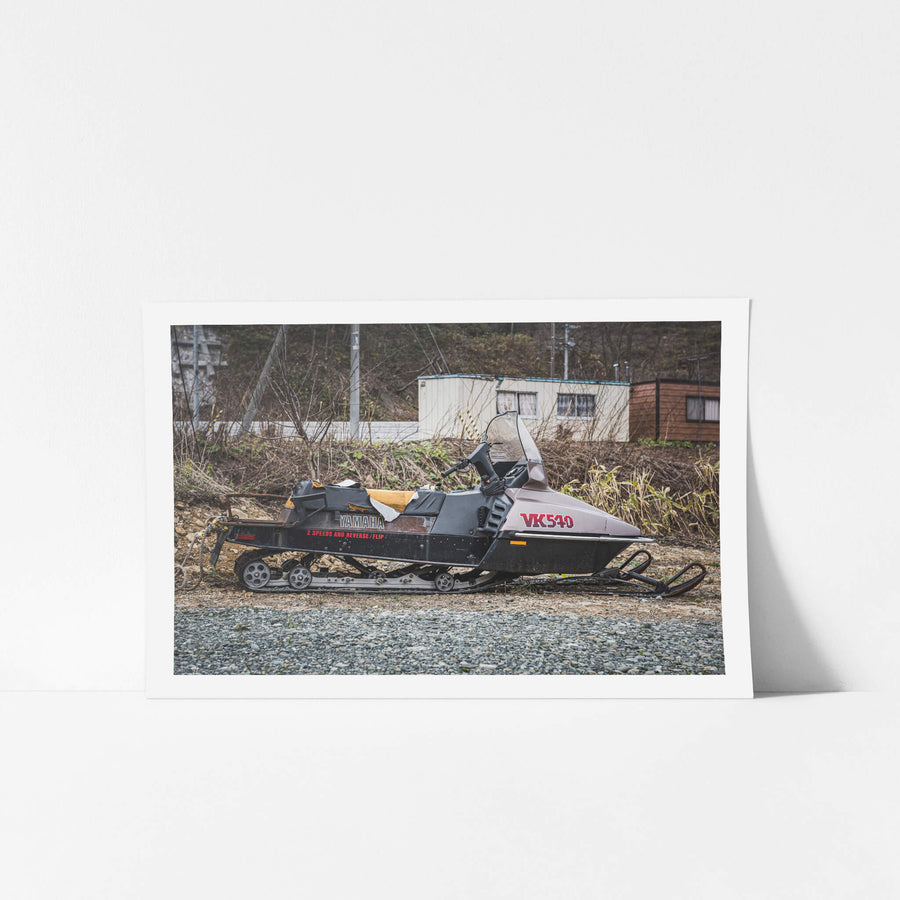 Snowmobile at Streetscapes of Yubari, a Yamaha VK540 snowmobile sits on bare gravel beside a quiet road.