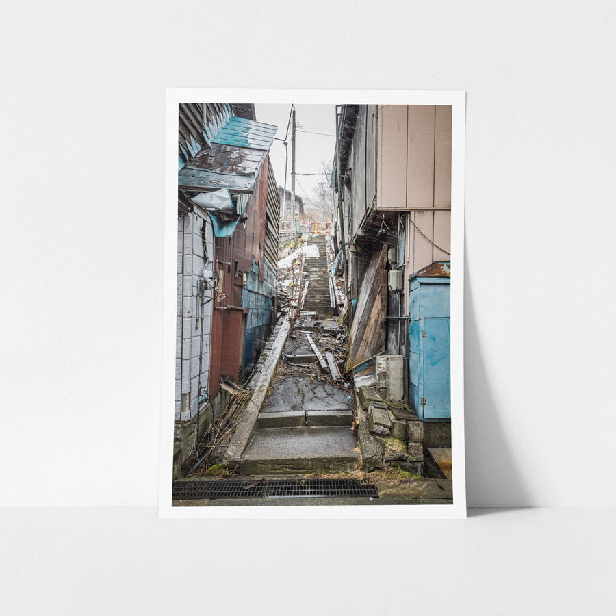Stairway at Streetscapes of Yubari, a narrow concrete stairway climbs steeply between tightly packed buildings.