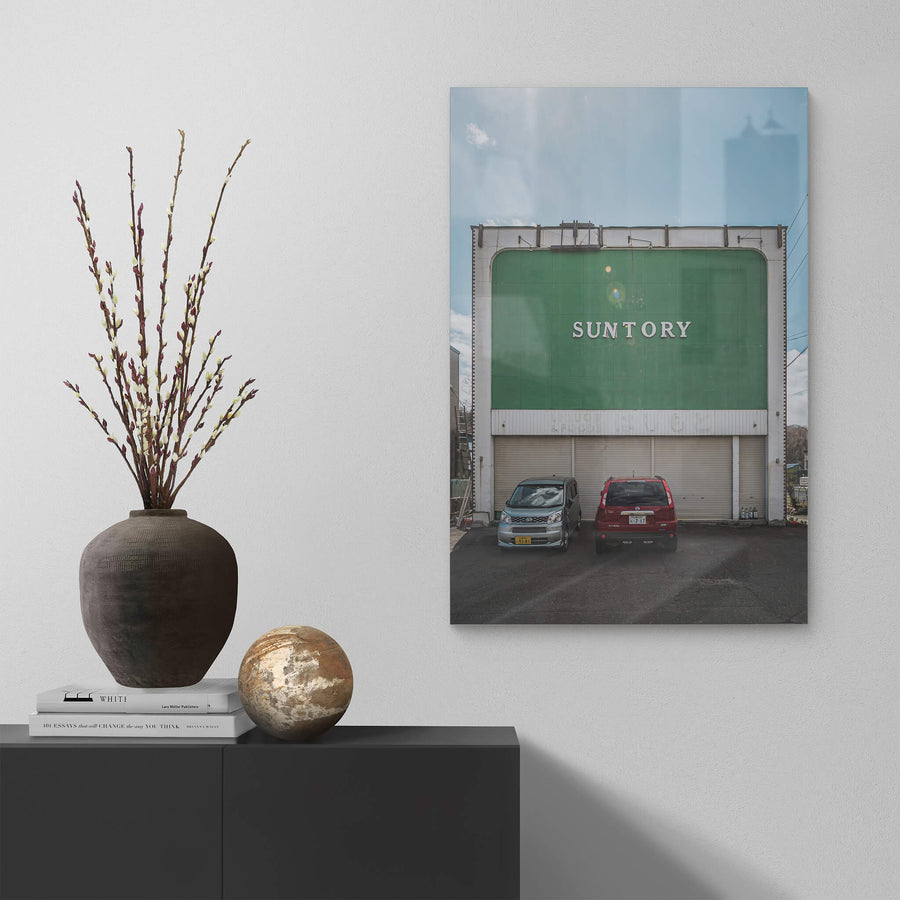 Suntory at Streetscapes of Yubari, a broad green façade rises two storeys above a small asphalt lot.