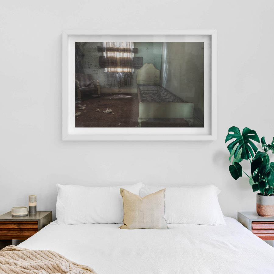 Guest Room at Terminus Hotel, a single bed frame sits along the wall, its bare springs exposed, beside a worn armchair.