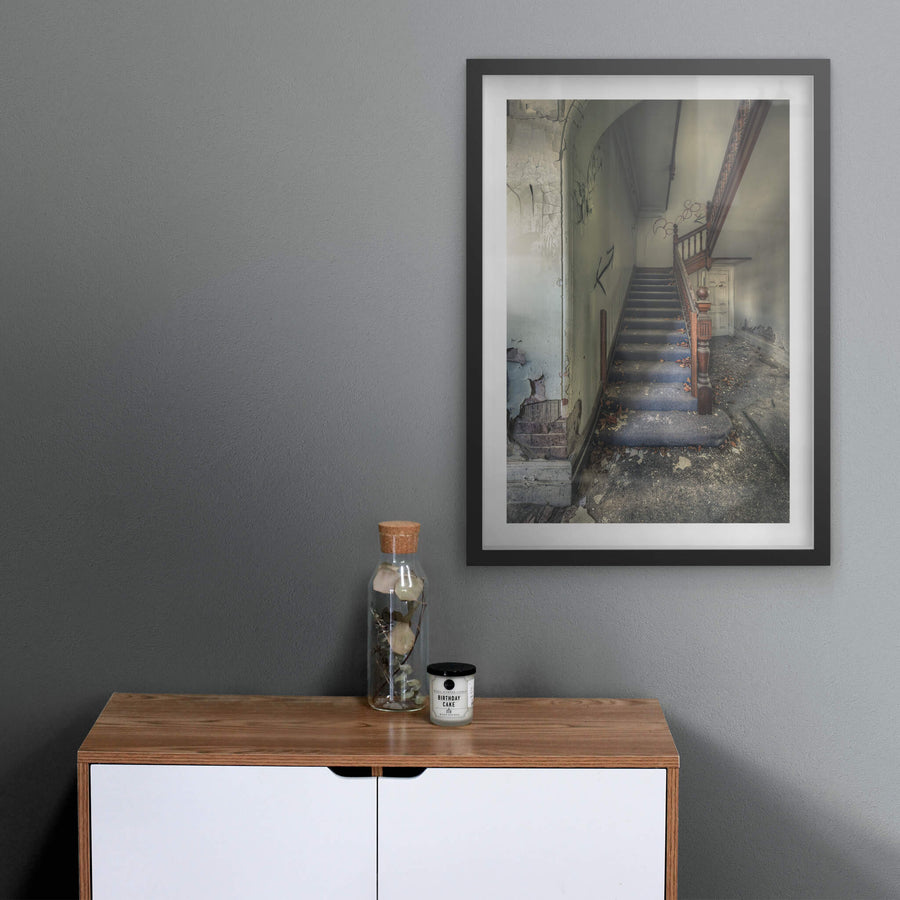 Crumbling Stairwell at The Asylum, a carved timber newel post stands at the base of a carpeted staircase.