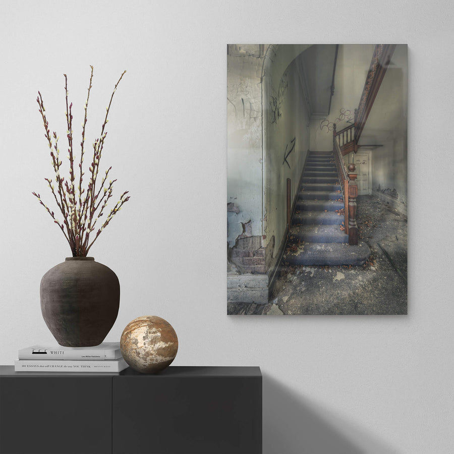 Crumbling Stairwell at The Asylum, a carved timber newel post stands at the base of a carpeted staircase.