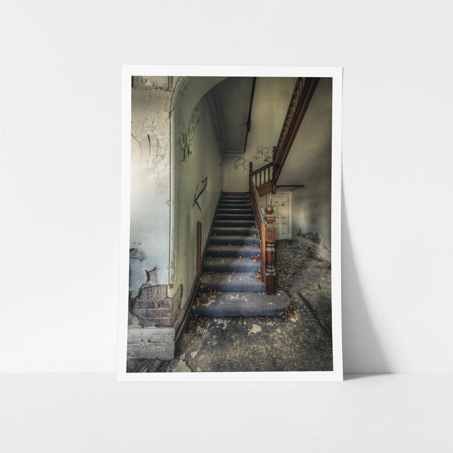 Crumbling Stairwell at The Asylum, a carved timber newel post stands at the base of a carpeted staircase.