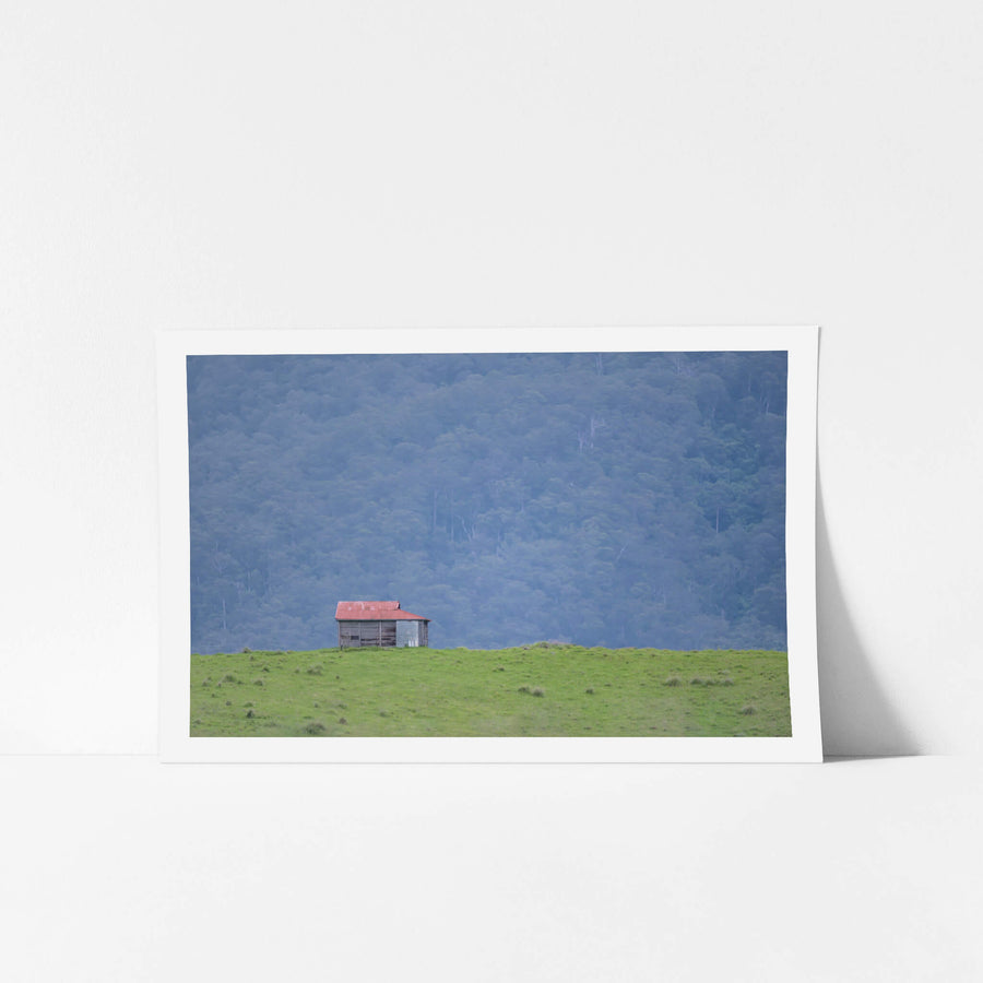 Brown Mountain Backdrop at The Dairy, a single timber and corrugated iron hut sits on a green ridge, small against.