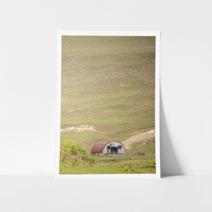 Nissen Hut In The Distance at The Woolshed, a Nissen hut sits at the base of a vast open hillside, dwarfed by the slope.