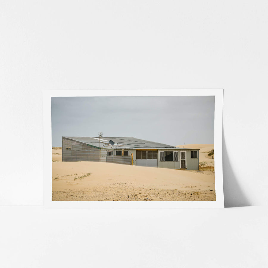 Sloped Roof at Tin City, a corrugated iron shack sits half-swallowed by sand.