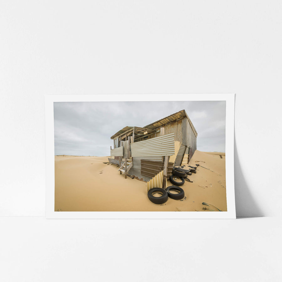 Tyres at Tin City, a corrugated iron shack lists sideways into a dune, its verandah posts leaning at odd angles.