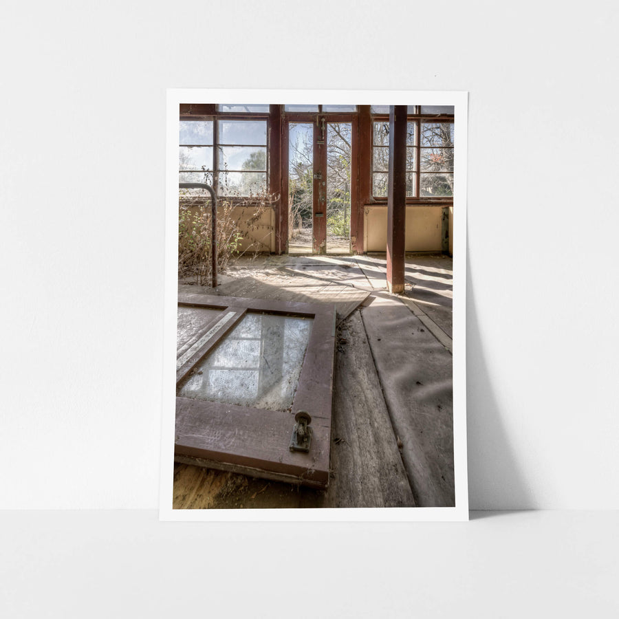 Breaking Down The Doors at Waterfall Sanatorium, a timber door lies flat on the floorboards, its glass panel still intact.