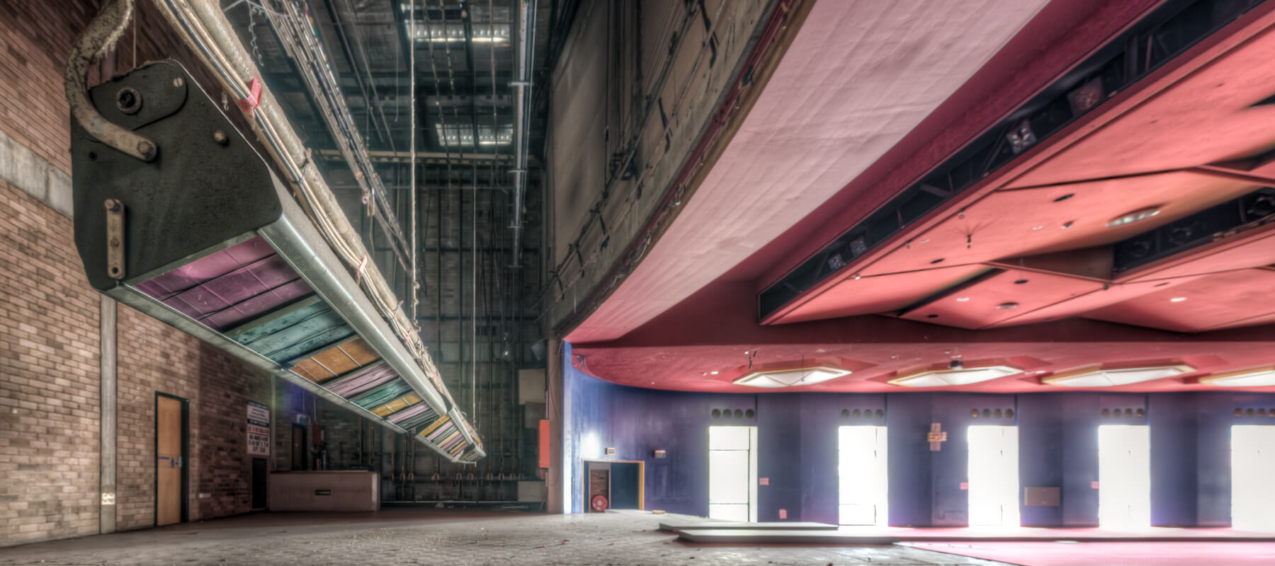 Interior of the abandoned Bankstown RSL auditorium, showcasing its vibrant red ceiling, colorful stage rigging, and empty performance space before demolition. Captured by Lost Collective.
