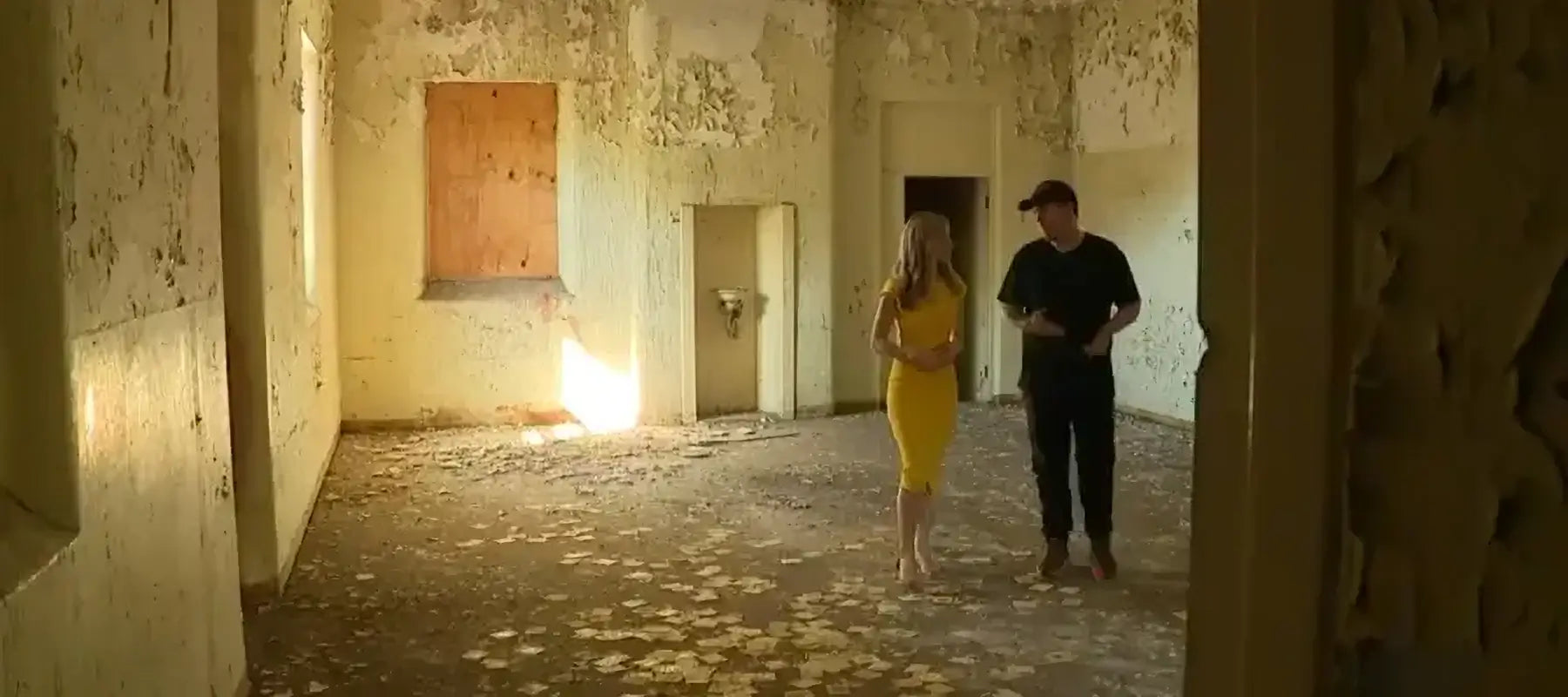 Brett Patman and Samantha Brett walk through a decaying room inside Callan Park, surrounded by peeling paint and crumbling walls, during a 7News Sydney feature on Lost Collective.