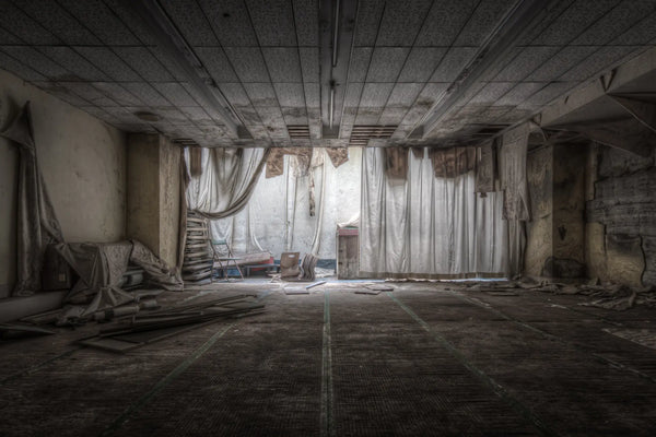An empty function room inside Kinugawa Kan, cream fabric drapes fallen from the ceiling, a step ladder against the back wall, debris scattered across the grid-tiled floor.