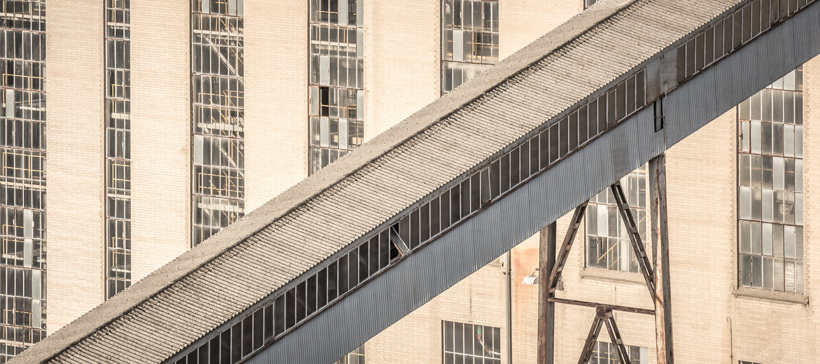 Abstract close-up of an industrial conveyor system at an abandoned power station, with its textured roof and glass-panelled building facade in the background.