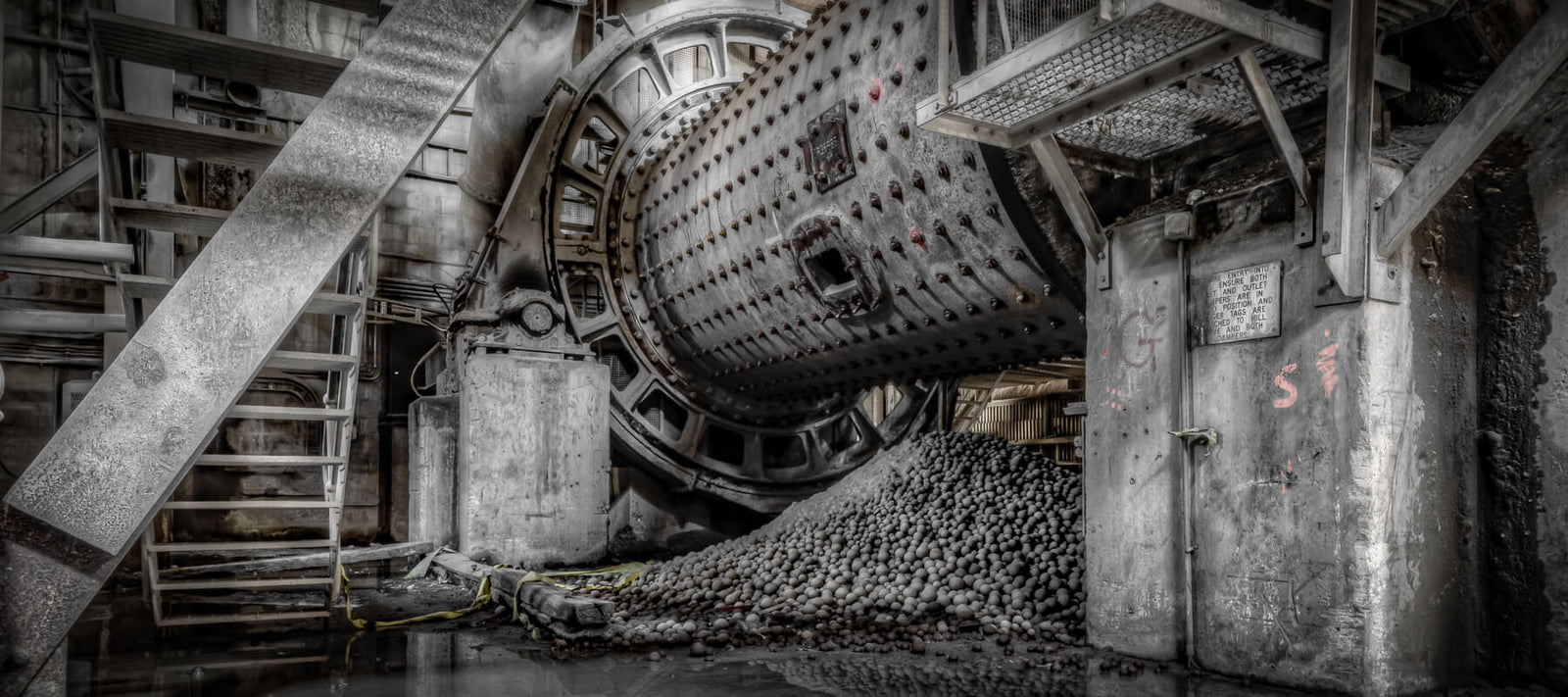 Interior of Kandos Cement Works featuring an industrial ball mill surrounded by concrete stairs, metal structures, and piles of grinding media, showcasing the site’s historic industrial architecture.