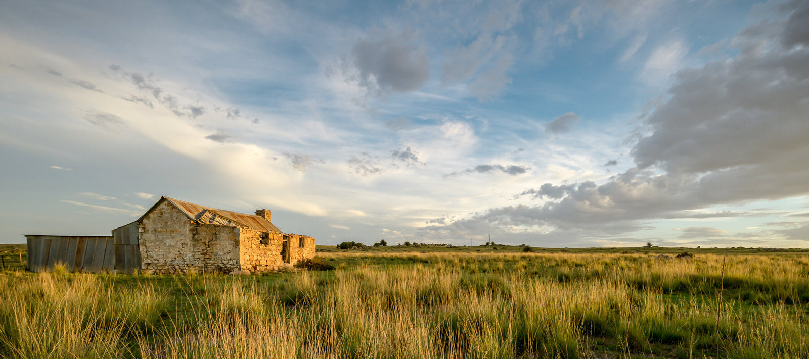 Abandoned rural homestead amidst Australian grasslands under a dramatic sky.