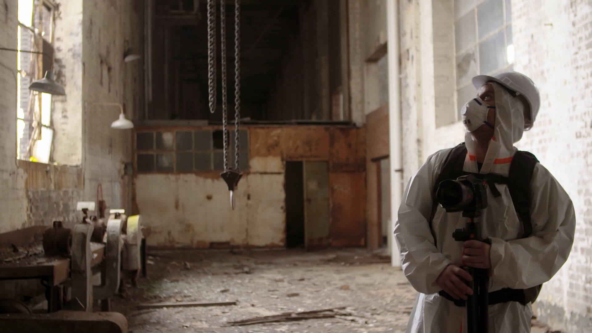 Brett in protective gear exploring an abandoned industrial building, surrounded by decayed machinery and aged brick walls.