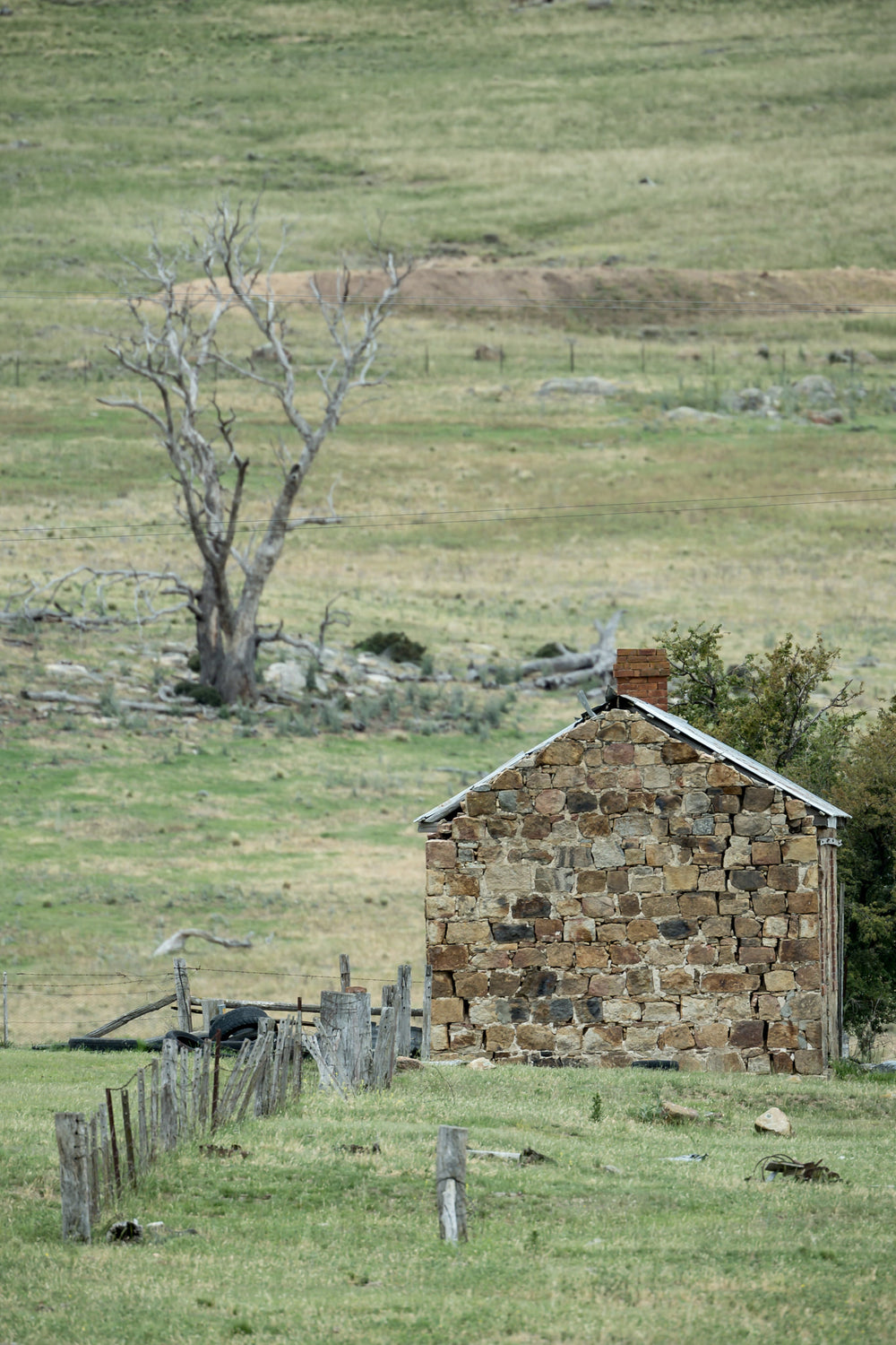 Jindabyne Hut at A Place to Call Home, a stone cottage sits low in open pastoral land near Jindabyne.