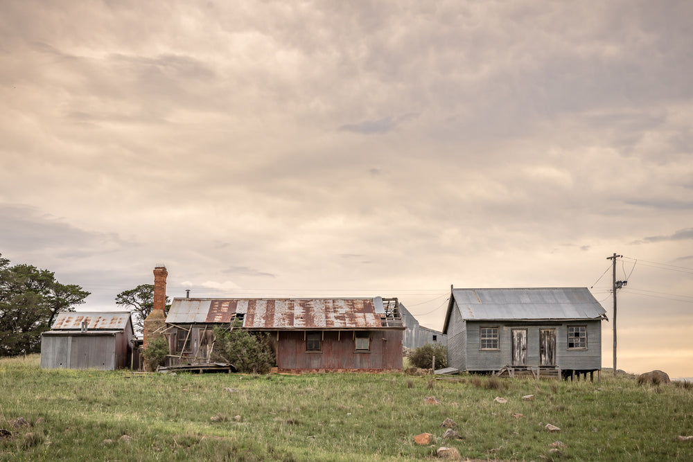 Numbla Vale Buildings at A Place to Call Home, a cluster of buildings sits on a green rise under heavy, layered cloud.