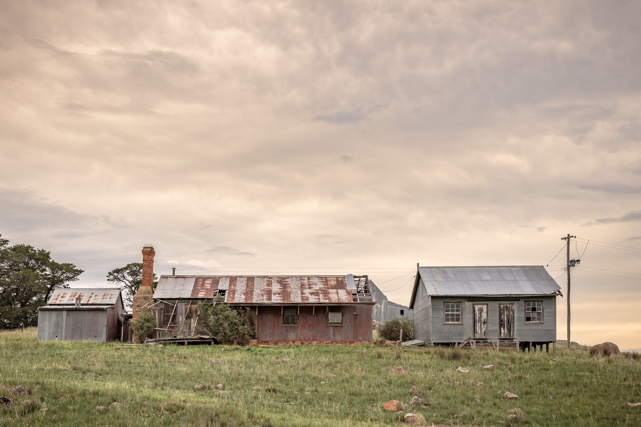 Numbla Vale Buildings at A Place to Call Home, a cluster of buildings sits on a green rise under heavy, layered cloud.
