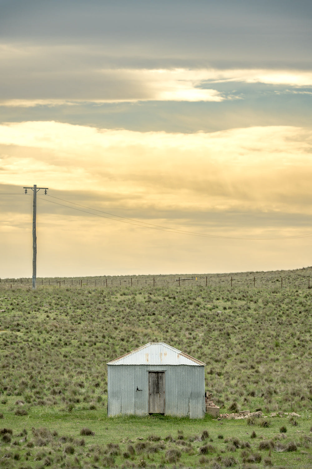 Springfield Drovers Hut at A Place to Call Home, a single corrugated iron hut sits low in open grassland.
