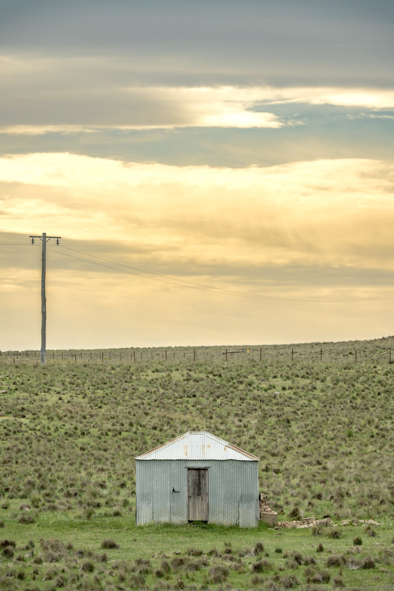 Springfield Drovers Hut at A Place to Call Home, a single corrugated iron hut sits low in open grassland.