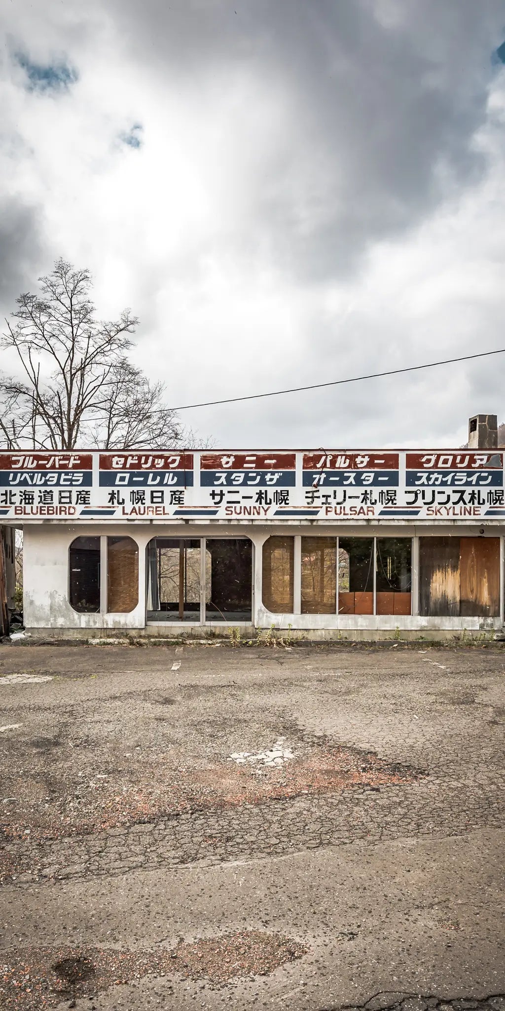 Abandoned car dealership in Hokkaido, Japan, with weathered signage and overgrown surroundings. A haunting yet beautiful representation of urban decay.