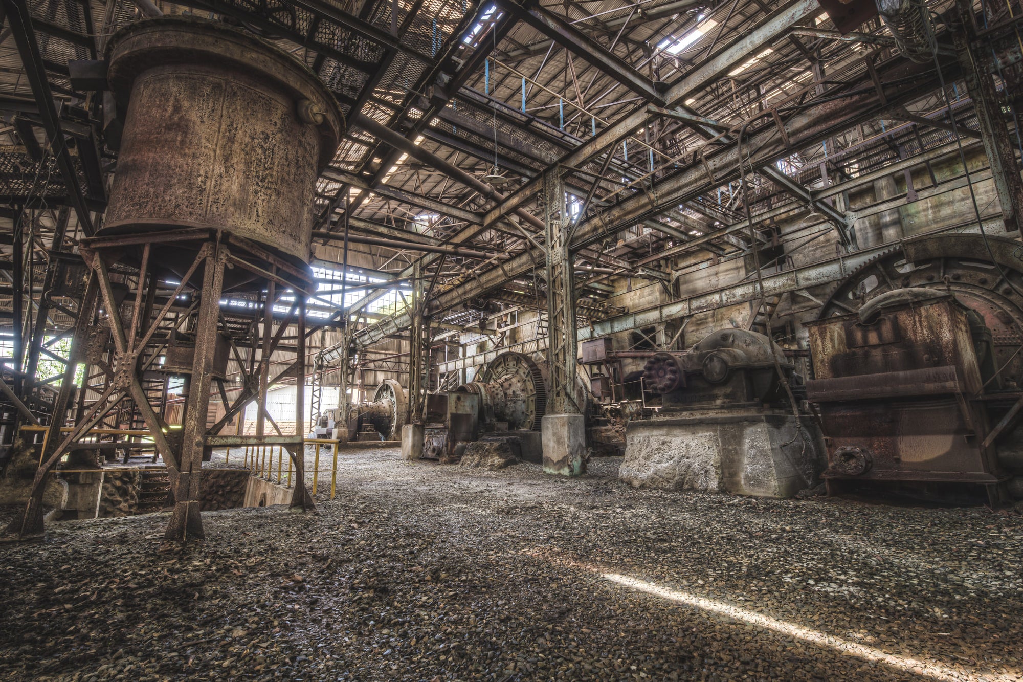 Ball Mills at Ashio Copper Mine, a cylindrical hopper rises on steel legs to the left, rust coating every surface in deep.