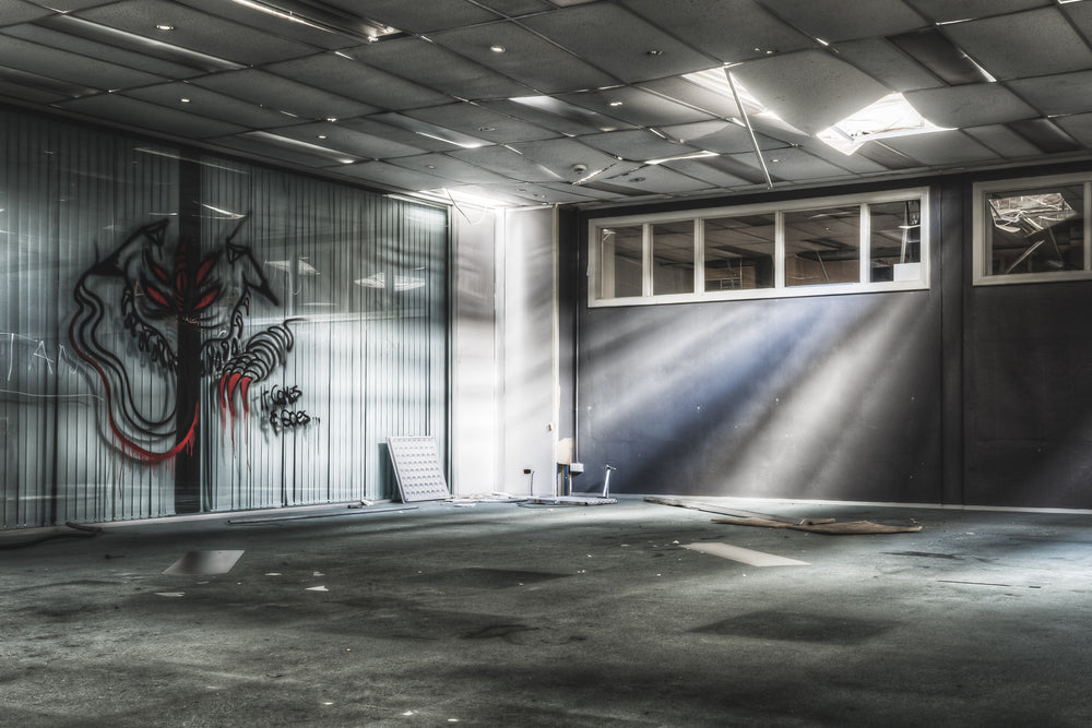 Office at ATL Building, a suspended ceiling sags where panels have collapsed, letting sharp beams of daylight cut.