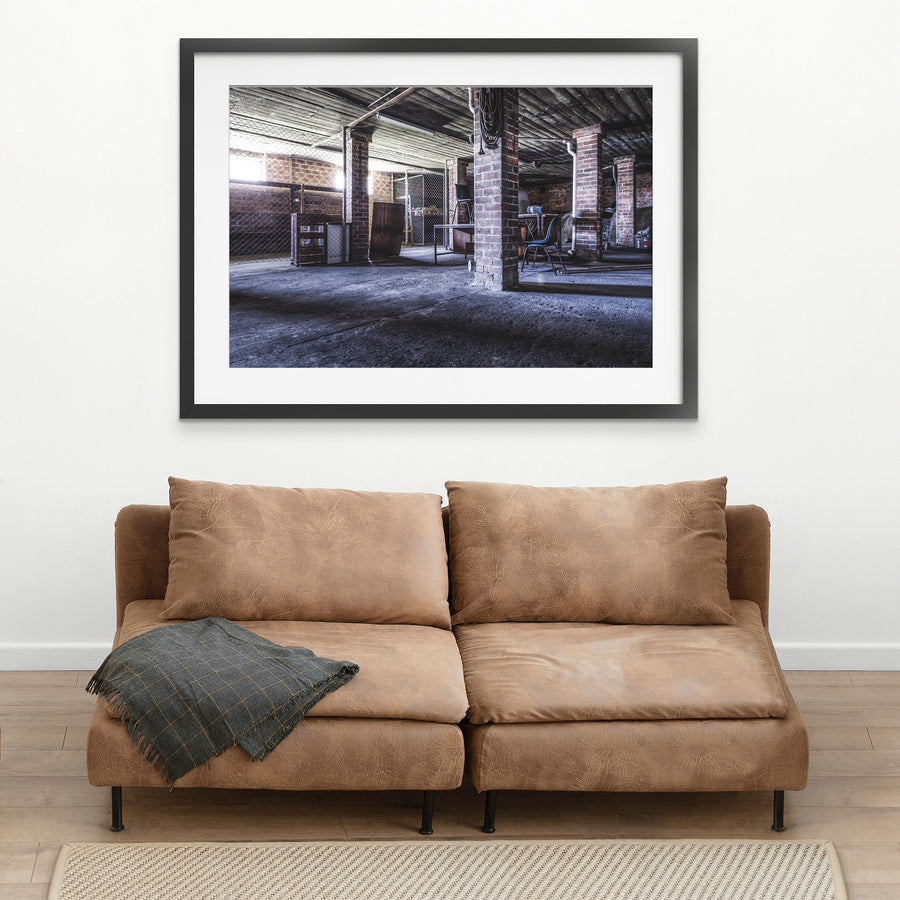 A coiled rope hangs from a brick column in the basement of the administration building at Awaba Colliery, with an overturned office chair on a desk and shadows across the concrete floor.