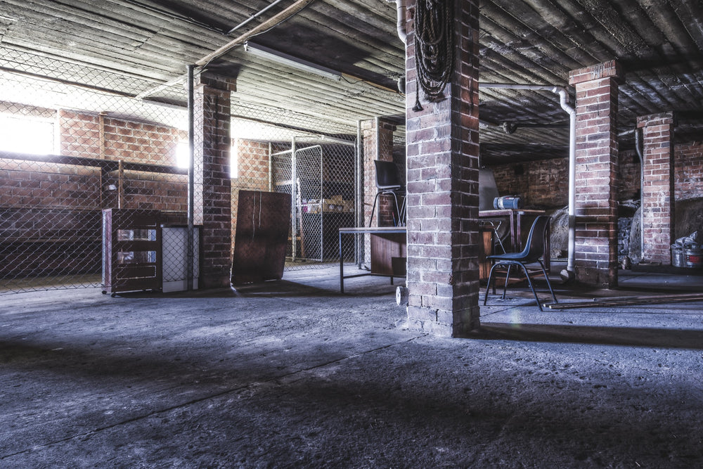 A coiled rope hangs from a brick column in the basement of the administration building at Awaba Colliery, with an overturned office chair on a desk and shadows across the concrete floor.