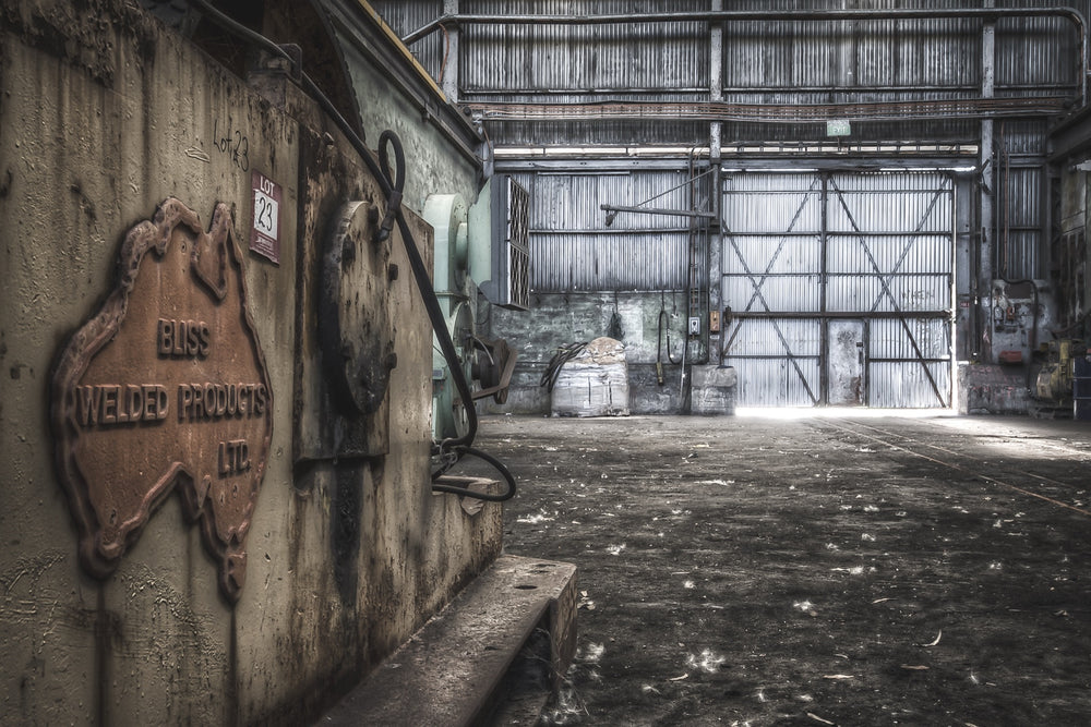 A conveyor drive casing with a 'LOT 23' label affixed, inside a surface building at Awaba Colliery, with bright light pushing through a corrugated metal door at the far end.