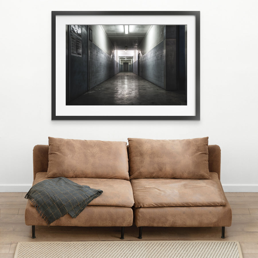 A narrow corridor at Awaba Colliery with fluorescent lights still burning along the ceiling, light-grey tiled walls, a concrete floor, and a closed door at the far end.