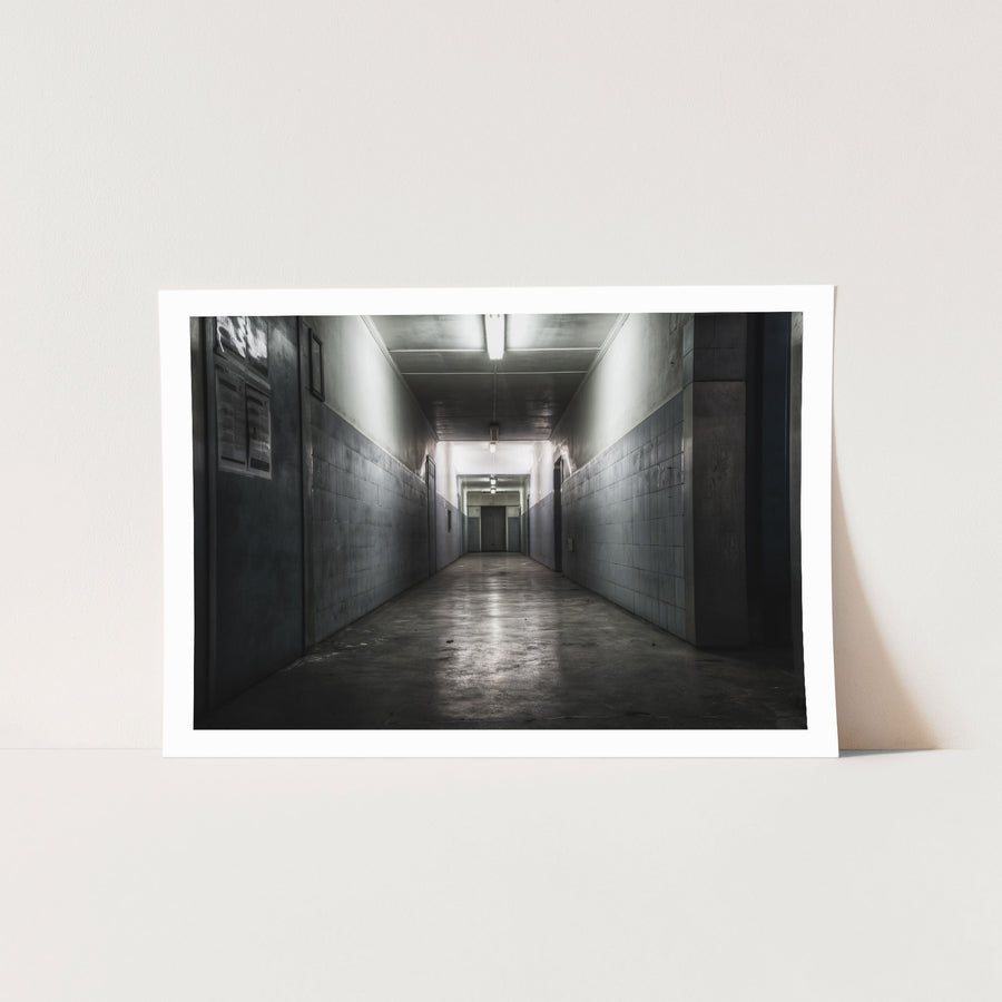 A narrow corridor at Awaba Colliery with fluorescent lights still burning along the ceiling, light-grey tiled walls, a concrete floor, and a closed door at the far end.