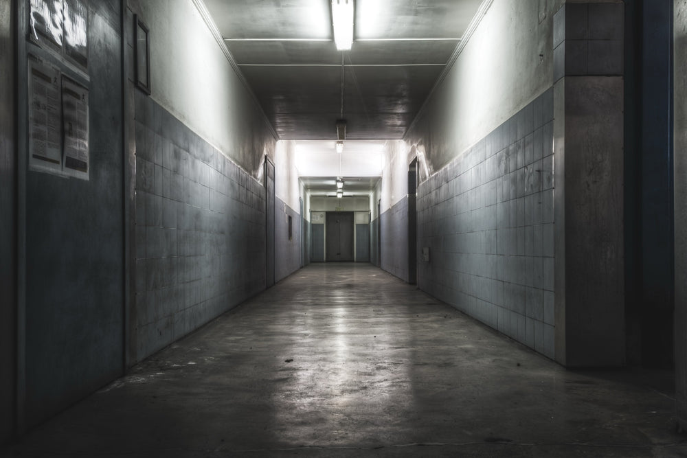 A narrow corridor at Awaba Colliery with fluorescent lights still burning along the ceiling, light-grey tiled walls, a concrete floor, and a closed door at the far end.