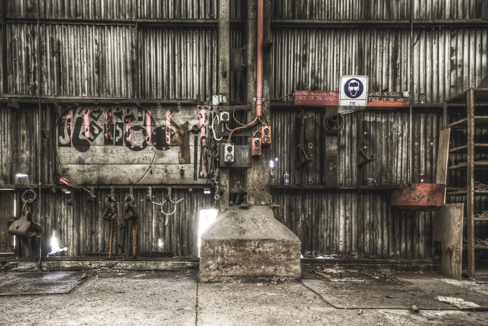 Workshop wall at Awaba Colliery showing a pegboard with remaining lifting gear, an empty grinder base, red safety signs, and graffiti on wooden planking.