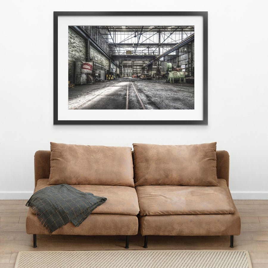 Rusted cylindrical machinery and twin rail tracks on the workshop floor at Awaba Colliery, with a Johnson-Hepburn sign hanging from a gantry crane and grease buckets lining the left wall.