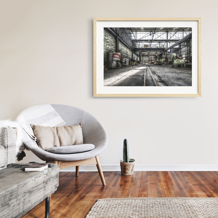 Rusted cylindrical machinery and twin rail tracks on the workshop floor at Awaba Colliery, with a Johnson-Hepburn sign hanging from a gantry crane and grease buckets lining the left wall.