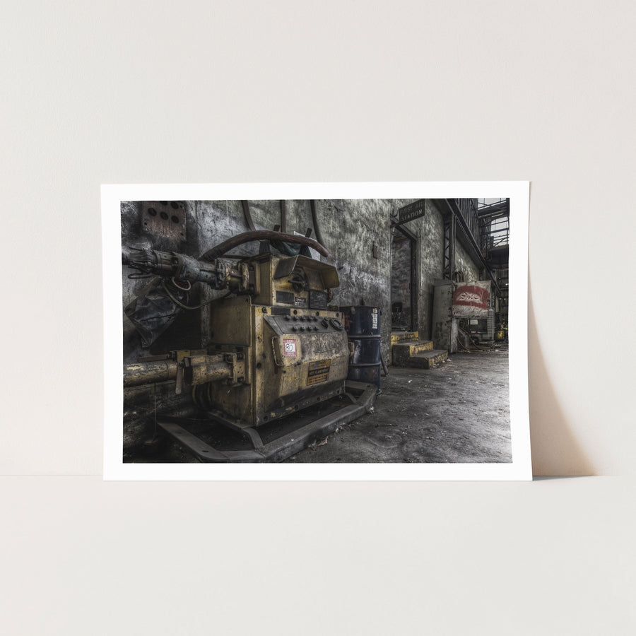 A yellow slurry pump tagged 'Lot 80' with control knobs and pipework in the interior of Awaba Colliery, blue barrels stacked against the wall and a First Aid Station doorway visible in the background.