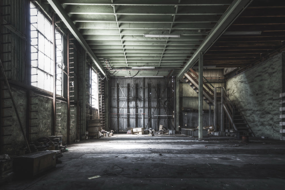 Steel storage racks, sprocket drives on the floor, and what appear to be PLC units near a timber staircase inside the stores building at Awaba Colliery, photographed in 2015.