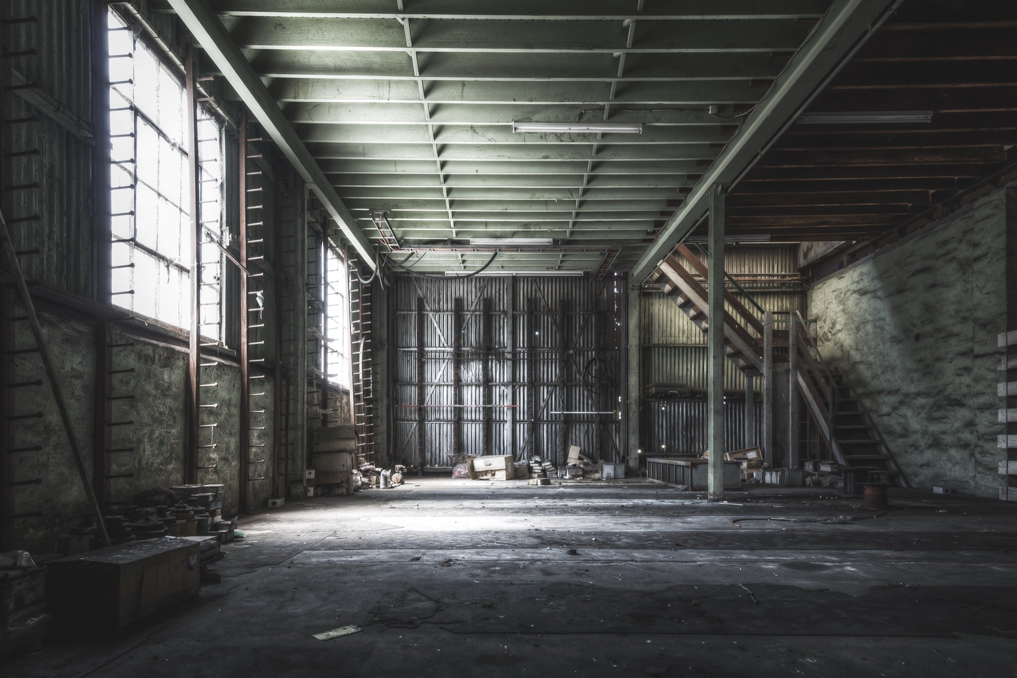 Steel storage racks, sprocket drives on the floor, and what appear to be PLC units near a timber staircase inside the stores building at Awaba Colliery, photographed in 2015.