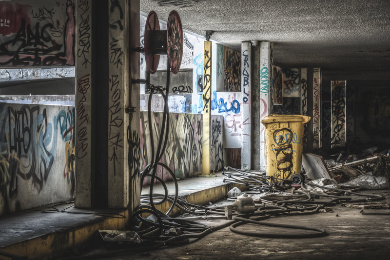 Two red hose reels are fixed to a concrete column inside the former Balmain Leagues Club at Rozelle, both catching what light reaches this level. A graffiti-tagged yellow bin sits in the middle distance.