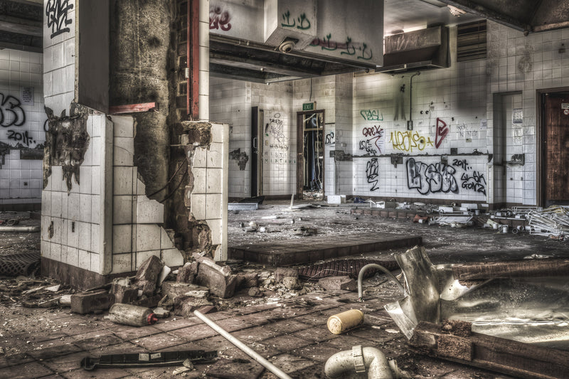 The former kitchen at Balmain Leagues Club, Rozelle, unlit and stripped. Broken tiles cling to a column in the foreground, exposing brick and bent rebar beneath.