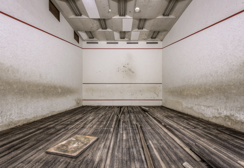 Squash Court at Bankstown RSL, the hardwood floor has buckled and warped, planks lifting away from the subfloor in long.