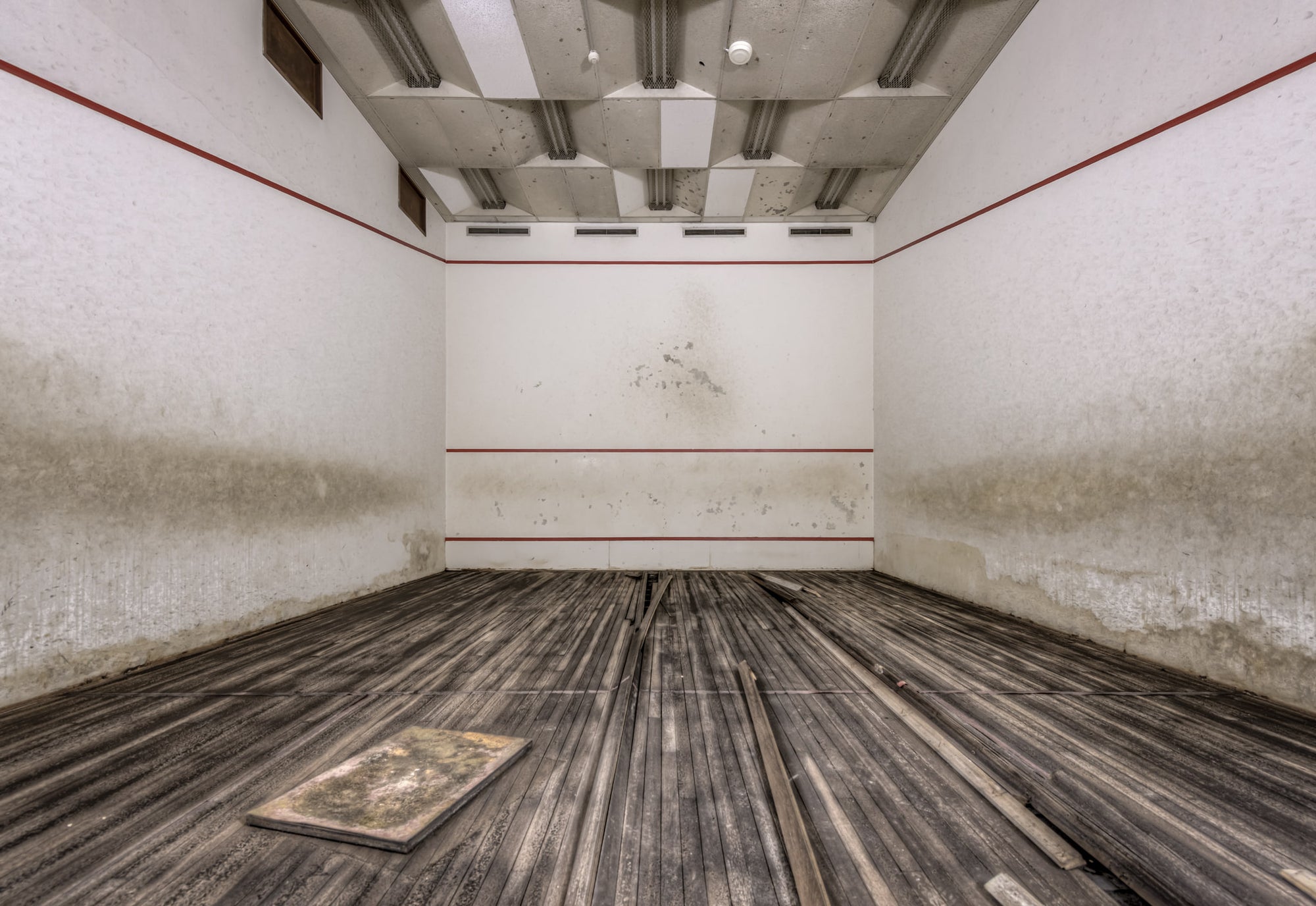 Squash Court at Bankstown RSL, the hardwood floor has buckled and warped, planks lifting away from the subfloor in long.