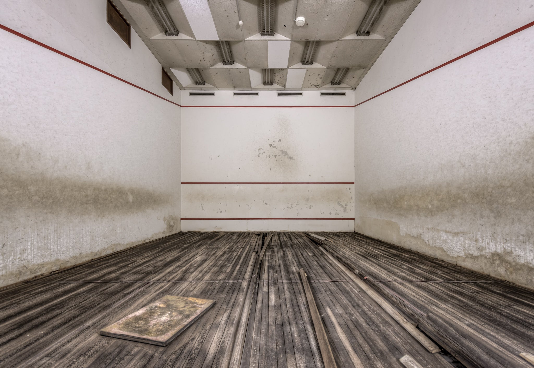 Squash Court at Bankstown RSL, the hardwood floor has buckled and warped, planks lifting away from the subfloor in long.