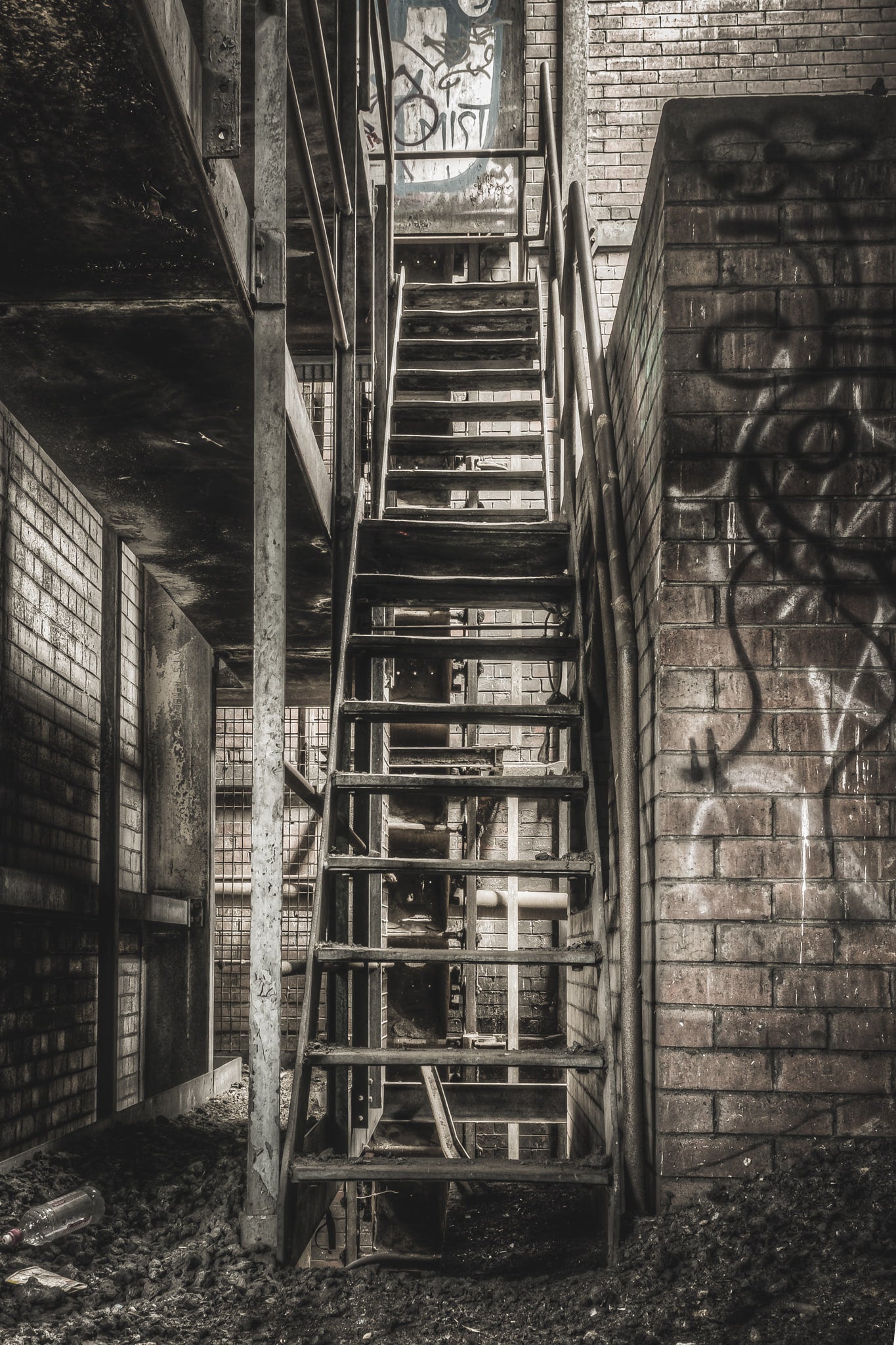 Stairs To Level Two at Bathurst Gasworks, a steel staircase climbs between brick walls, bolted to a narrow column.