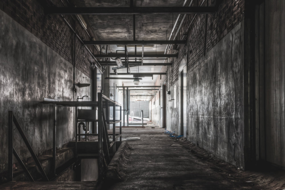Downstairs Exit at Blayney Abattoir, a concrete corridor narrows toward a mesh gate at the far end, where grey light spills.