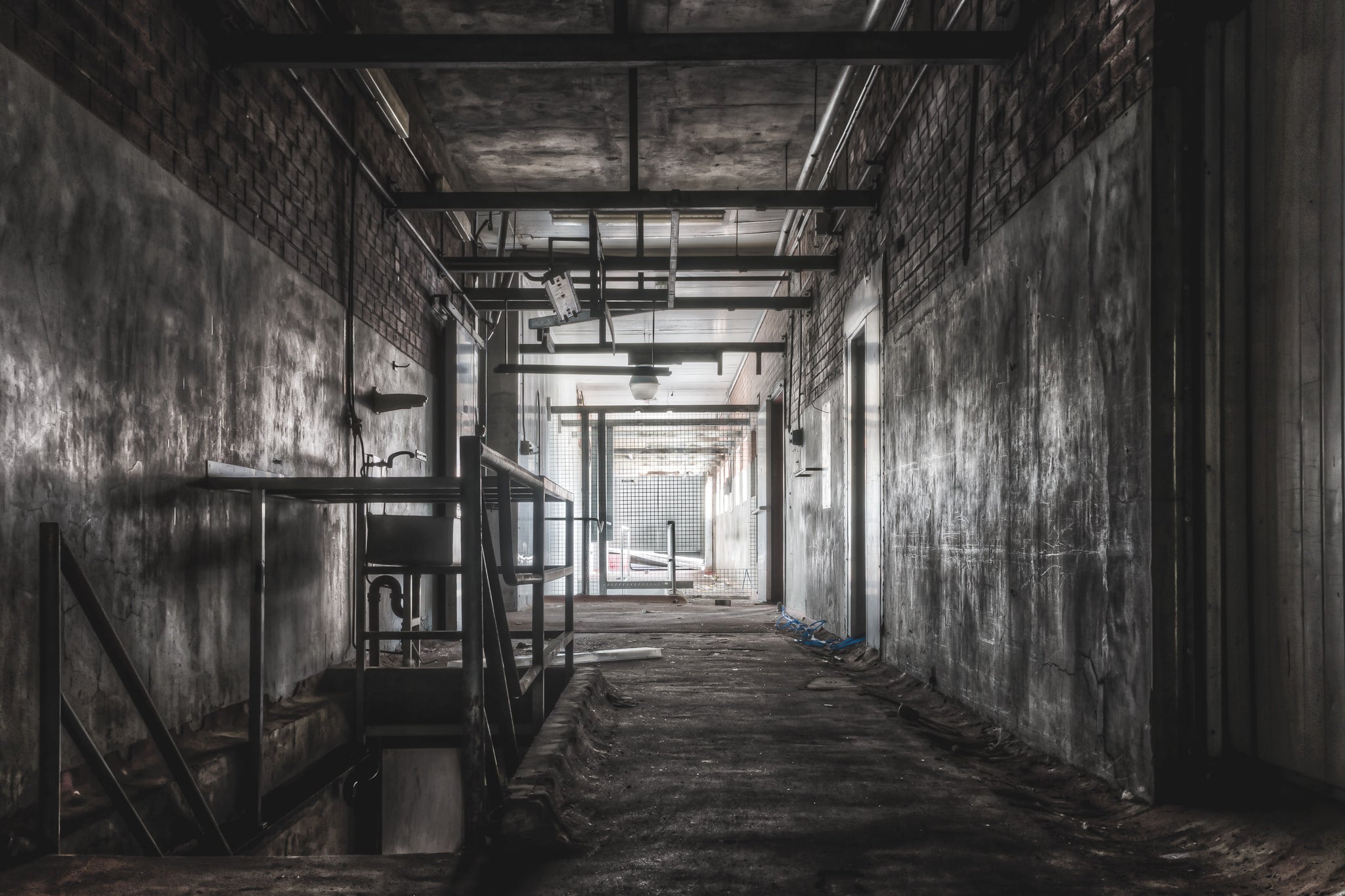 Downstairs Exit at Blayney Abattoir, a concrete corridor narrows toward a mesh gate at the far end, where grey light spills.